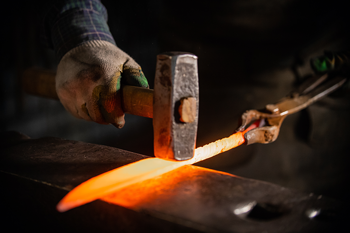 Blacksmith striking red-hot knife steel with hammer on anvil