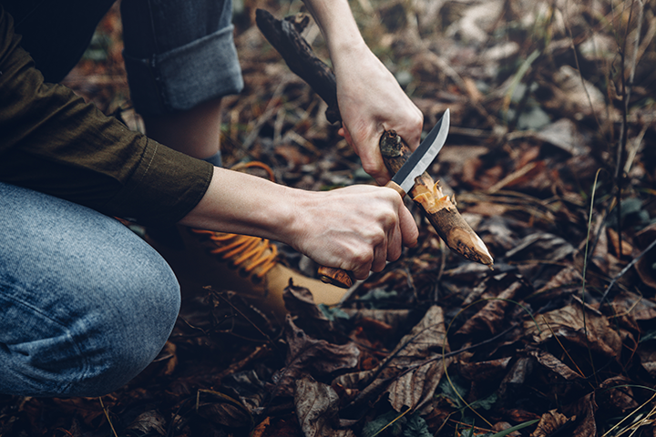 man-in-blue-jeans-cutting-stick-with-bushcraft-knife